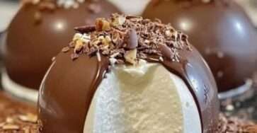 Dômes glacés à la vanille recouverts d’une coque en chocolat brillant, décorés d’éclats de fruits secs.