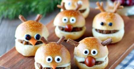 Mini burgers apéritifs décorés en rennes de Noël avec fromage fondu, olives noires, tomates cerises et bretzels salés.
