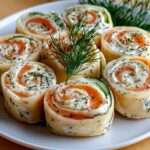 Roulés au saumon fumé et fromage frais aux herbes, coupés en spirales régulières et dressés sur un plateau festif.