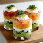 Verrines d’avocat crémeux, yaourt grec onctueux et saumon citronné, garnies d’aneth frais et de dés de concombre.