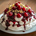 Pavlova aux cerises fraîches nappée d’un coulis noir épais, crème fouettée vanillée et éclats de chocolat noir.