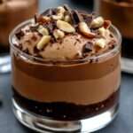 Mini verrines de mousse au chocolat noir aérienne, sur base biscuit chocolat, garnies d’éclats de noisette et copeaux de chocolat.