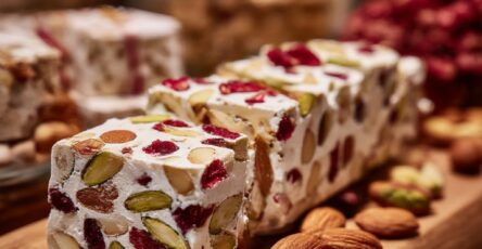 Nougat blanc artisanal aux amandes torréfiées, pistaches vertes et cranberries rouges, découpé en tranches régulières.