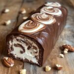 Bûche roulée au chocolat garnie de crème vanillée, recouverte d’une ganache brillante et décorée de fruits secs.