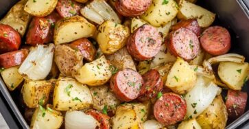 Plat familial de saucisses fumées en rondelles et pommes de terre grenaille rôties au four avec oignons caramélisés et persil frais ciselé