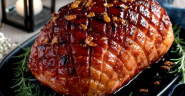 Rôti de porc glacé au miel, ail et romarin, doré et caramélisé au four, tranché sur une planche avec jus de cuisson brillant