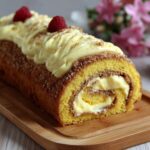 Bûche roulée garnie de crème de marrons et crème chocolat blanc, décorée de noix de coco et framboises, montrant une spirale régulière à la découpe