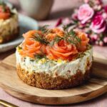 Mini cheesecake salés garnis de saumon fumé roulé en rosaces et d’aneth frais, présentés en petites portions individuelles sur une assiette