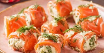Roulés de saumon fumé garnis de fromage frais et d’aneth, découpés en bouchées et disposés sur un plat de service