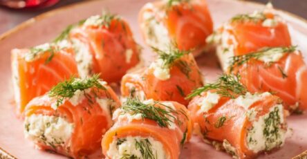 Roulés de saumon fumé garnis de fromage frais et d’aneth, découpés en bouchées et disposés sur un plat de service