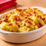 Gratin de pommes de terre doré au four avec lardons, fromage fondant et baies roses sur le dessus dans un plat à gratin