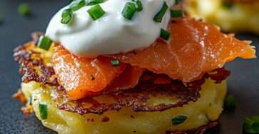 Galettes de pommes de terre dorées et croustillantes, surmontées de saumon fumé et nappées de crème à la ciboulette, servies chaudes dans une assiette