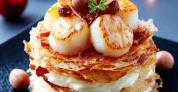 Millefeuille salé composé de feuilletage doré, crème de panais onctueuse et noix de Saint-Jacques dorées, décoré de noisettes et chips de chorizo