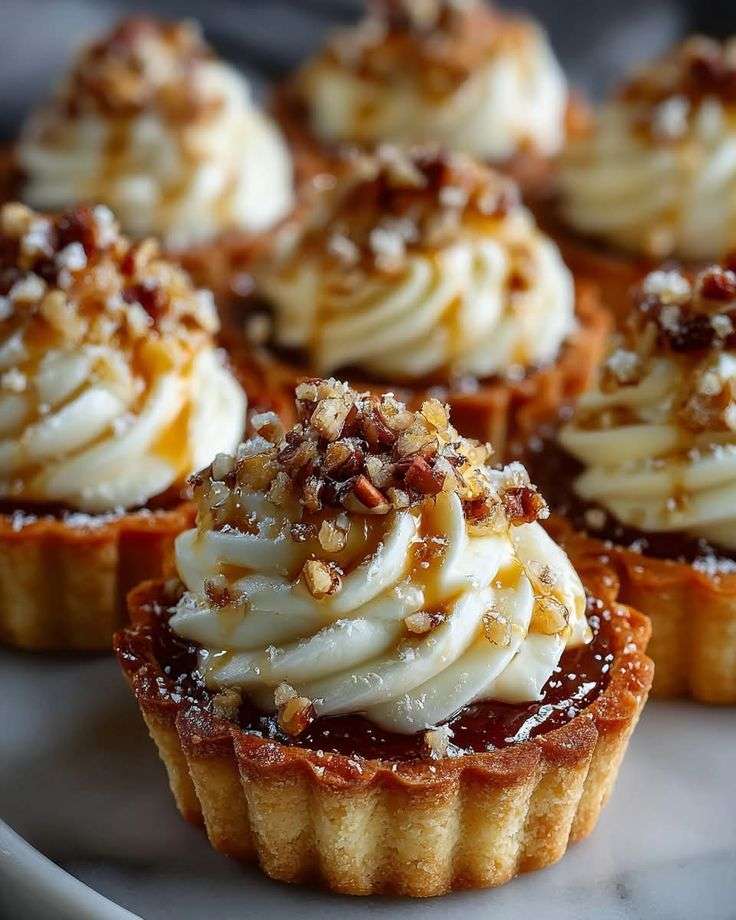 Mini tartelettes au fromage à la crème avec pacanes croquantes et filet de sirop d’érable.