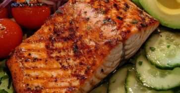 Salade de saumon grillé doré, tranches d’avocat mûr, concombre croquant, tomates cerises et vinaigrette citronnée dans une assiette blanche.