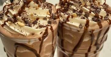 Grand verre de milkshake au chocolat crémeux décoré de sirop de chocolat, garni de crème fouettée, pépites de chocolat et éclats de noix