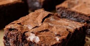 Brownie fondant au chocolat noir coupé en carrés, texture dense et moelleuse, surface légèrement craquelée, servi sur une assiette en bois.