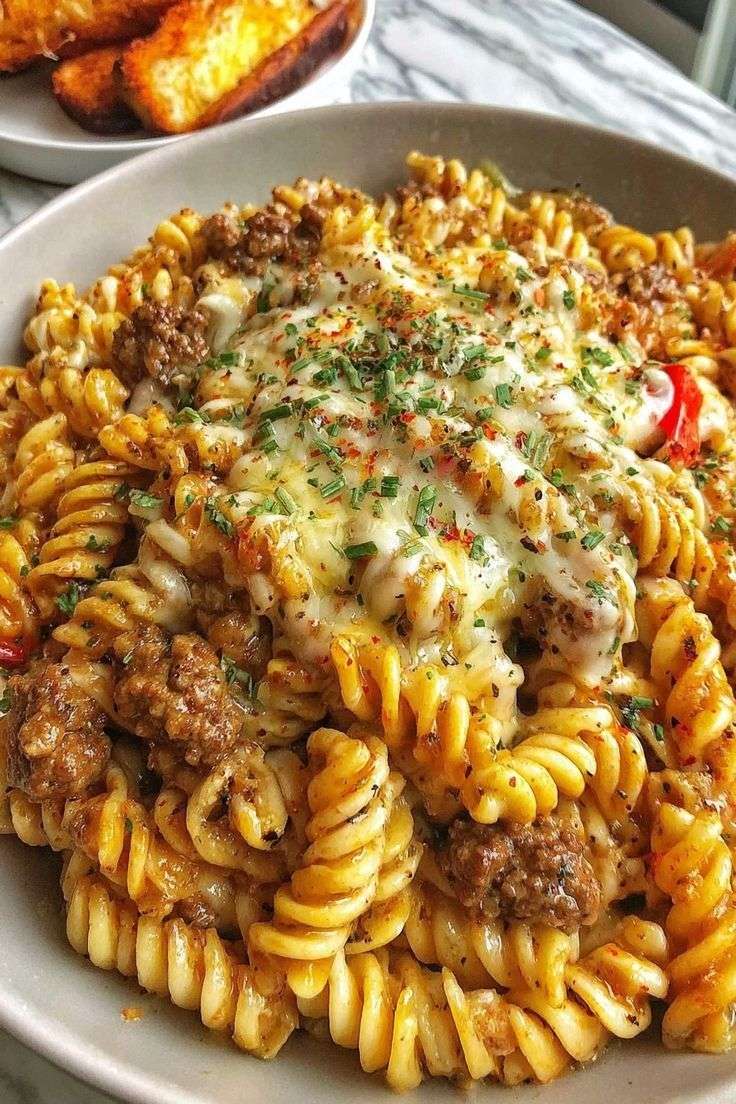Assiette de fusillis crémeux au bœuf haché et fromage fondu, sauce tomate crémeuse, garnie de persil frais, servie chaude sur table en bois.