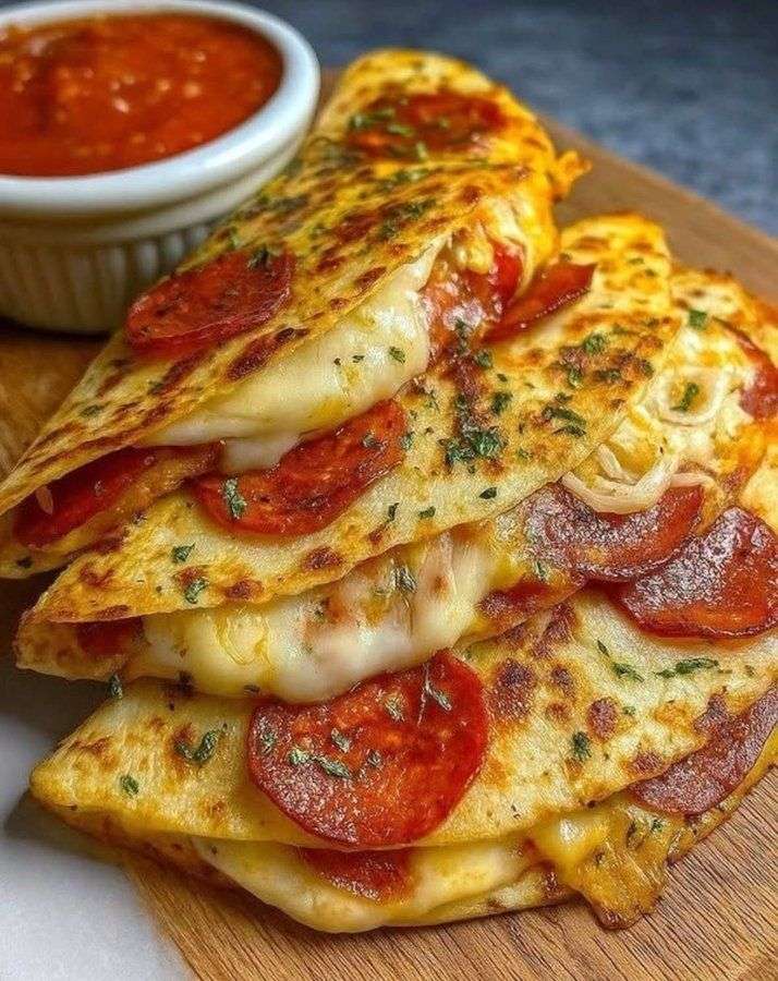 Quesadilla façon pizza garnie de mozzarella fondante, pepperoni croustillant et sauce tomate, coupée en parts dorées sur planche en bois.