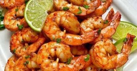 Brochettes de crevettes grillées dorées au citron vert et paprika fumé, garnies de coriandre fraîche, servies avec quartiers de lime.