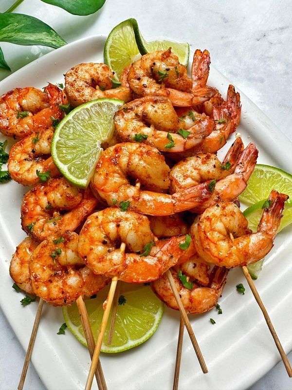 Brochettes de crevettes grillées dorées au citron vert et paprika fumé, garnies de coriandre fraîche, servies avec quartiers de lime.