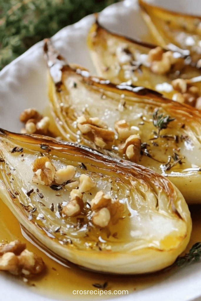 Endives rôties au four nappées de miel, parsemées de noix de Grenoble et thym frais, dorées et caramélisées dans un plat rustique.