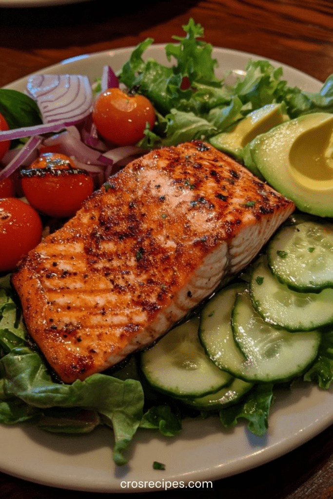 Salade de saumon grillé doré, tranches d’avocat mûr, concombre croquant, tomates cerises et vinaigrette citronnée dans une assiette blanche.