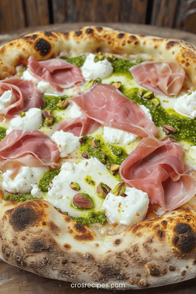 Pizza dorée au four garnie de pesto vert, burrata fondante, tranches fines de prosciutto et pistaches concassées, arrosée d’huile d’olive et décorée de basilic frais.