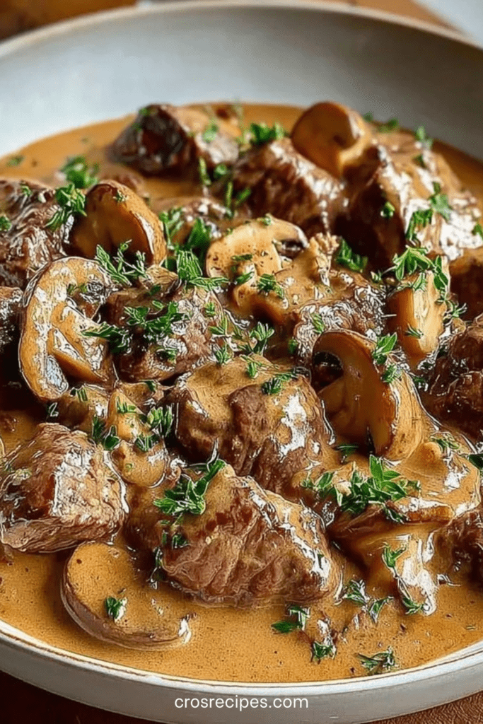 Bœuf Stroganoff crémeux aux champignons servi chaud dans une poêle, morceaux de bœuf tendres nappés de sauce onctueuse, persil frais et champignons dorés.