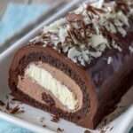 Bûche roulée au chocolat nappée d’un glaçage brillant, garnie d’un cœur vanille visible à la coupe et décorée de copeaux de chocolat noir et blanc