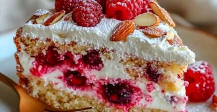 Gâteau au yaourt revisité aux framboises garni de crème légère et d’amandes effilées, présenté sur un plat avec texture moelleuse et fruits frais.