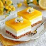 Carrés mousse mangue et vanille avec base biscuitée, couche vanille onctueuse, mousse mangue aérienne et nappage brillant, décorés de fleurs comestibles.