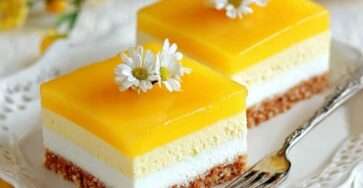 Carrés mousse mangue et vanille avec base biscuitée, couche vanille onctueuse, mousse mangue aérienne et nappage brillant, décorés de fleurs comestibles.