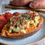 Patate douce farcie aux lardons et fromage fondu, gratinée au four, garnie de tomates cerises et persil frais, servie chaude.