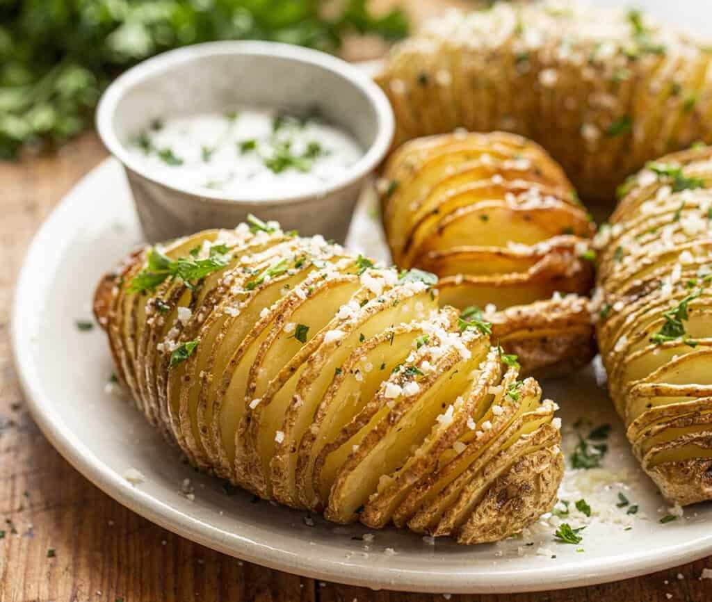 Pommes de terre Hasselback dorées et croustillantes au four, entaillées en accordéon, badigeonnées de beurre, ail et herbes fraîches.