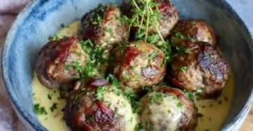 Boulettes de bœuf à la moutarde ancienne nappées de sauce crémeuse, servies chaudes dans une poêle avec herbes fraîches et texture fondante.