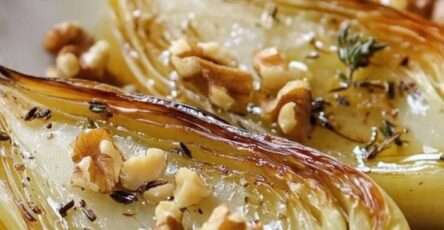 Endives rôties au four nappées de miel, parsemées de noix de Grenoble et thym frais, dorées et caramélisées dans un plat rustique.