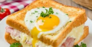 Croque-madame doré au four avec jambon blanc, fromage fondu et œuf au plat coulant, servi chaud avec herbes fraîches.