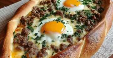 Pide turque en forme de bateau garnie de viande hachée, fromage fondu et œufs coulants, cuite au four et parsemée de persil frais.