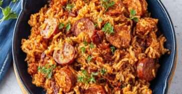 Riz au chorizo mijoté servi dans une poêle rustique, grains de riz fondants imprégnés de sauce tomate, rondelles de chorizo dorées et persil frais.