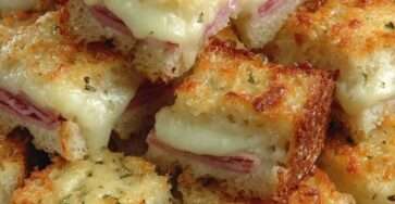 Cubes de croque-monsieur gratinés au four dans un plat, pain de mie doré et croustillant, jambon blanc, fromage fondu filant et herbes de Provence.