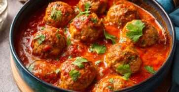 Boulettes de viande maison mijotées dans une sauce tomate épicée, servies chaudes avec herbes fraîches et pain pour saucer.