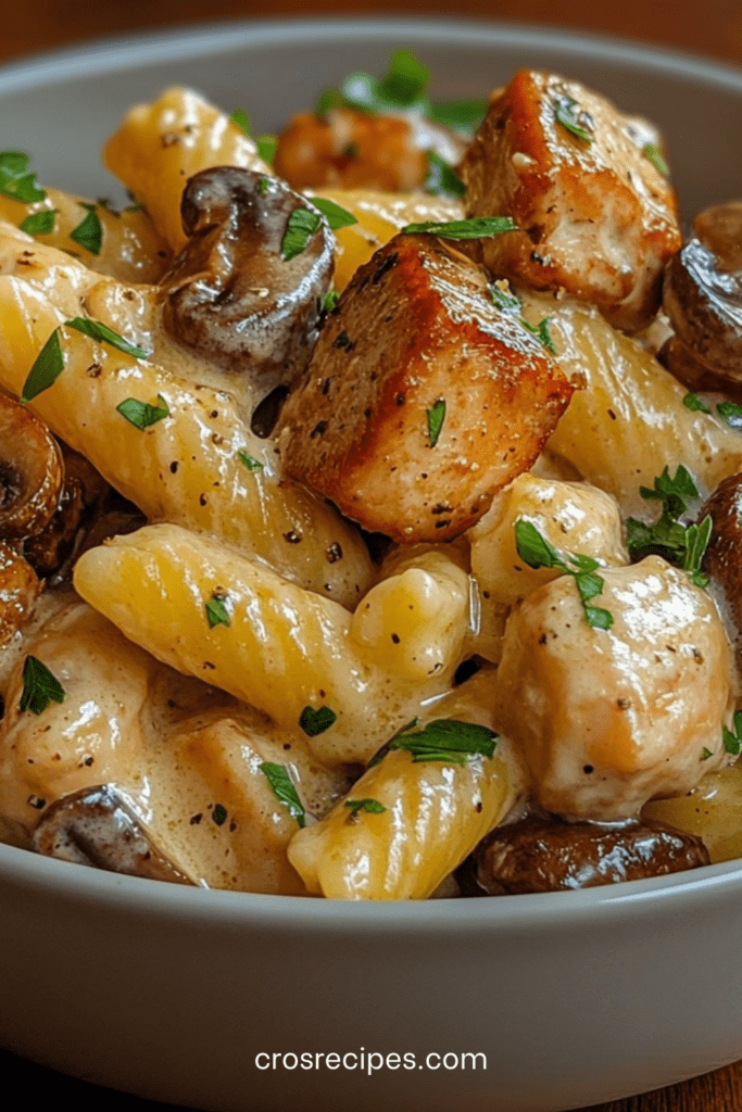 Assiette de pâtes crémeuses courtes au poulet et champignons nappées de sauce crémeuse, parsemées de parmesan et persil frais.