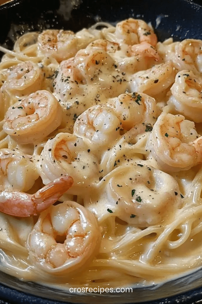 Assiette de pâtes crevettes Alfredo nappées d’une sauce crémeuse au parmesan, garnies de persil frais, servies chaudes dans une assiette blanche.