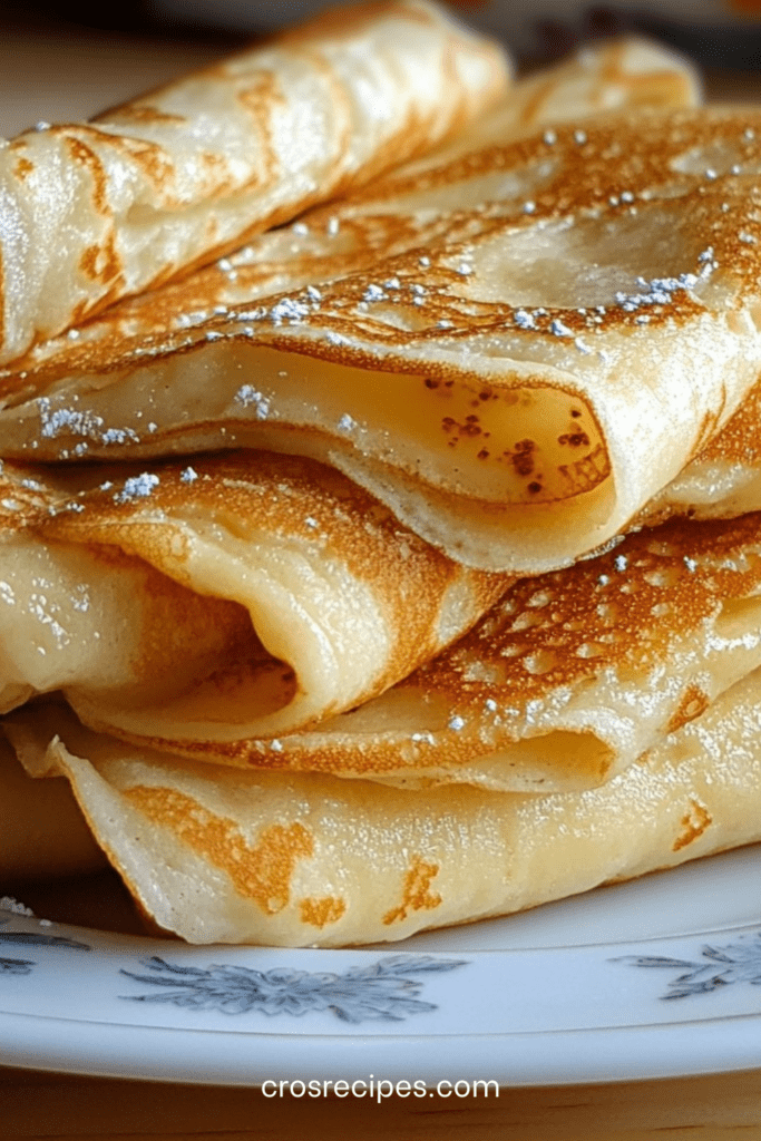 Pile de crêpes fines dorées et souples empilées sur une assiette, texture légère et régulière, prêtes à être garnies de sucre ou de confiture.