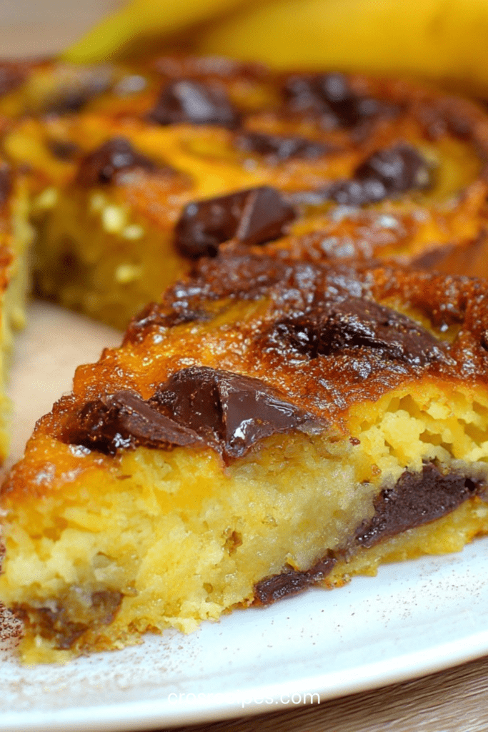 Clafoutis banane chocolat maison dans un moule beurré, bananes en rondelles et morceaux de chocolat noir fondants, surface dorée et légèrement gonflée à la sortie du four.