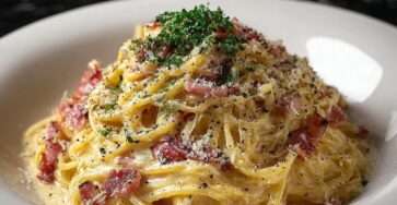 Spaghetti carbonara crémeux servis chauds avec pancetta croustillante, parmesan râpé et poivre noir, texture onctueuse visible et sauce brillante