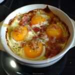 Œufs cocotte cuits au four en ramequins avec fromage de chèvre fondant, lardons fumés croustillants et jaune légèrement coulant.