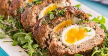 Pain de kefta marocain aux œufs, tranché et servi chaud, viande épicée fondante avec œufs au centre sur lit de verdure.