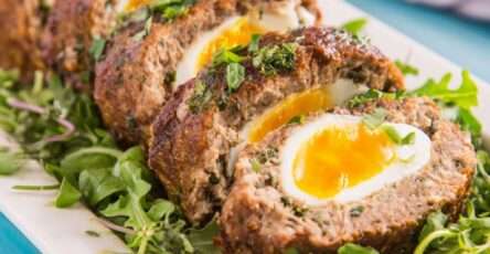 Pain de kefta marocain aux œufs, tranché et servi chaud, viande épicée fondante avec œufs au centre sur lit de verdure.